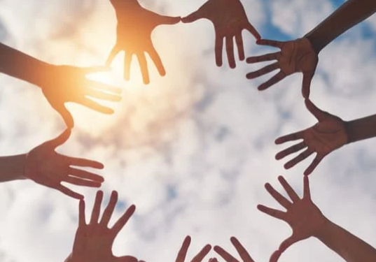 5 pairs of hands with fingers extended, forming a circle against the backdrop of a bright blue sky with white clouds.
